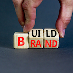 Build Your Brand Symbol. Concept Words Build Brand On Wooden Cubes. Businessman Hand. Beautiful Grey